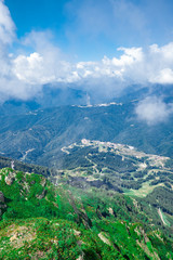 Landscape with mountains, lush green grass, lift and large caps of clouds over the mountain tops in Krasnaya Polyana, Sochi.