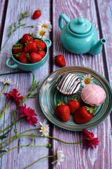Still life of bright juicy strawberries and cakes on a striped plate