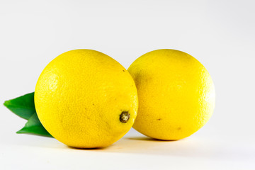 Two whole yellow lemons with green leaf isolated on white background