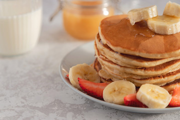 Close-up on a stack of pancake with banana and strawberry, drizzled with sweet syrup. Bright one. Space for text, Traditional American breakfast