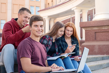 Happy smiling teenage boy with notebook against a group of students on the stairs near university