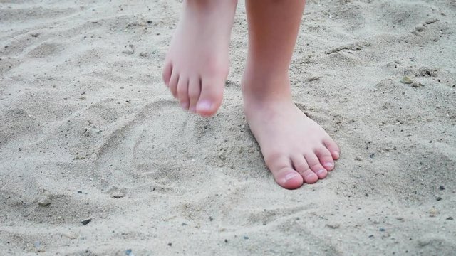 Two feet of a little boy standing still and marching on the sand place close up