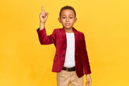 Attractive stylish Afro American schoolboy wearing elegant clothes raising fore finger as sign of drawing attention, making announcement, asking for silence. Body language, gestures and symbols