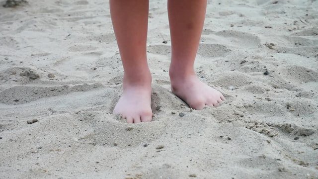 Two feet of a little boy pulling his toes out of the sand and walking away