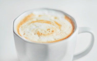 Light faceted cup with a delicate cappuccino with caramel and thick foam on a light background. An invigorating drink in the early morning.