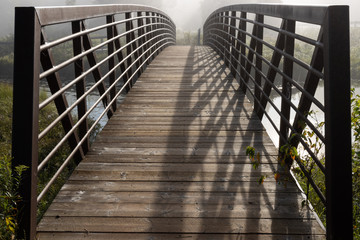 Wooden footbridge with iron bridge in early morning fog