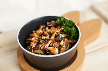 Delicious fried potatoes with chanterelles and onions in a black plate with a fork on a wooden stand in the form of a rabbit