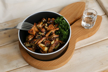 Delicious fried potatoes with chanterelles and onions in a black plate with a fork on a wooden stand in the form of a rabbit