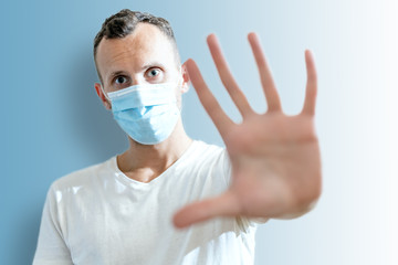 young man in medical mask shows open palm stop gesture on blue background