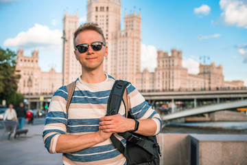 Naklejka premium Portrait of a young man in sunglasses with a backpack walking in the center of Moscow on the embankment