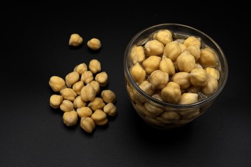 Chickpeas hydrating in a glass with water on black background