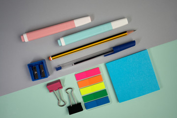 Top view of school supplies such as paperclips, notes, pen, pencil, pencil sharpener on a two-colored background