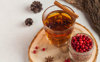 Hot tea with spices, Apple and berries in a transparent glass mug on a wooden stand. The concept of home comfort, autumn