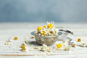 Dry chamomile flowers in infuser on white wooden table, closeup