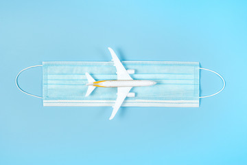 Plane model and face mask on a blue background. Flight impact of coronavirus (COVID-19) concept.