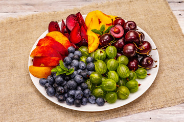 Assorted fresh berries of a cherry, gooseberry, blueberries, slices of ripe peach, plum and...