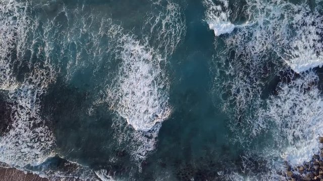 Waves consecutively lapping onto the shore and white bubbles remaining on the surface of beautiful blue ocean.