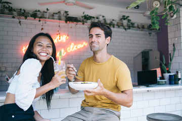 Portrait of cheerful multiracial male and female friends enjoying tasty food eating during lunch break having fun on conversation, happy woman and man couple in love satisfied with healthy nutrition