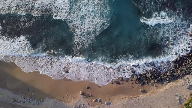 Waves consecutively lapping onto the shore and white bubbles remaining on the surface of beautiful blue ocean.