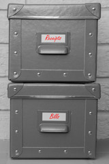 Storage boxes with receipts and bills written on labels in red.  With a grey brick background