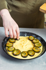 the chef's hand decorates a raw pie in a baking dish with plum halves