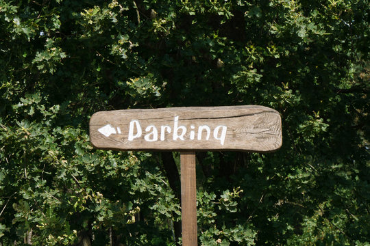 Parking wooden sign. Tourist outdoor destination arrow. Forest direction information. Summer camping in green park. Park your car over there signpost with white paint on brown desk.