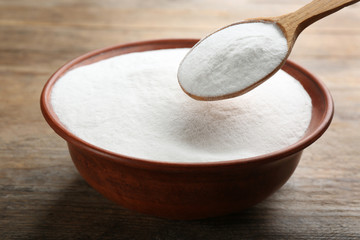 Baking soda in spoon and bowl on wooden table, closeup