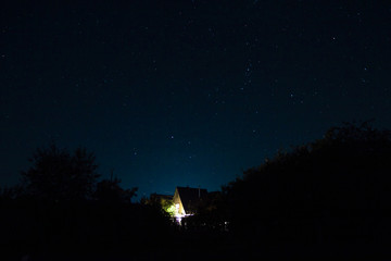 Starry night sky, and a wooden cottage with lights in the Windows