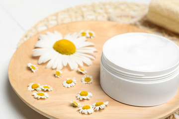 Fototapeta na wymiar Jar of cream and chamomiles on wooden plate, closeup