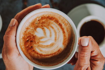 Hands holding fresh cappuccino coffee mug.
