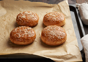 baked sesame buns on brown parchment paper, ingredient for a hamburger