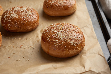 baked sesame buns on brown parchment paper, ingredient for a hamburger