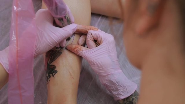 A woman in pink gloves makes a tattoo on the leg of a young girl. Tattoo studio. Slow motion.