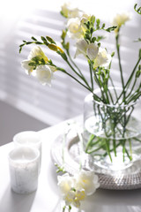Beautiful spring freesia flowers and candles on table in room