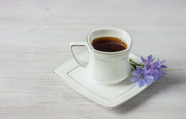 White cup of instant chicory drink or coffee with chicory flowers on a white table. Healthy food concept. Copy space.