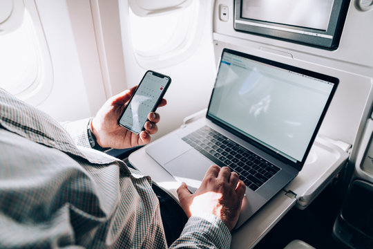 Man using smartphone and laptop in airplane