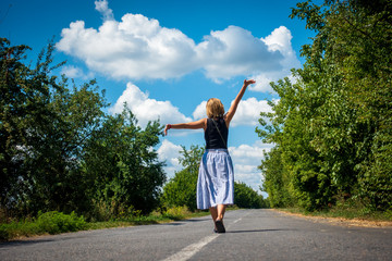 Happy girl walks along the carriageway. Trees grow along the road