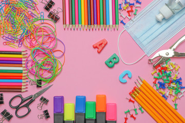 School stationery supplies with medical mask and hand sanitizer on pink background. Back to school and new normal concept. COVID-19 prevention.  Top view with copy space