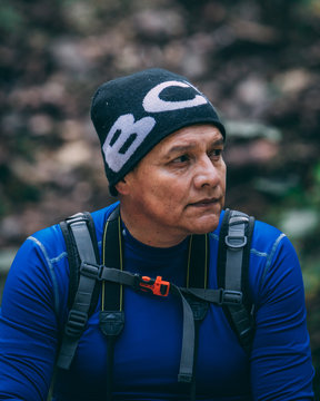 Old white man looking to the horizon on a green and cold forest background. Adult male with black bennie, black eyes and hiking gear. 