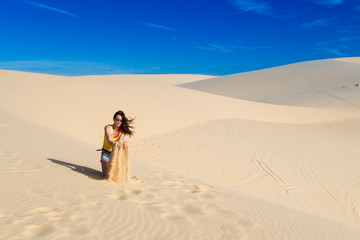 Woman in the desert, sitting on the sand, alone, playing with the sand.
