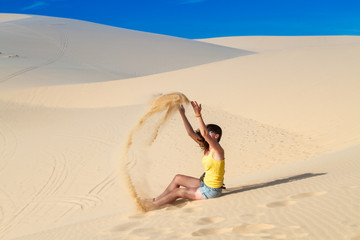 Woman throws sand while sitting in the desert on the sand