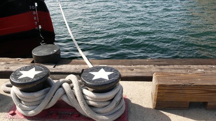Tied rope knot on metallic bollard with stars, seafaring port of San Diego, California. Nautical ship moored in dock. Cable tie fixed on wharf. Symbol of navy marine sailing and naval fleet, USA flag