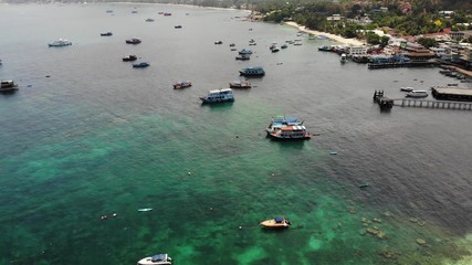 Boats in calm sea in port. Drone view of fishing and dive boats floating on tranquil surface of blue sea in harbor of tropical exotic paradise Koh Tao Island on sunny day in Thailand