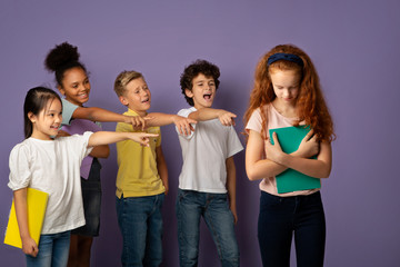Group of mean schoolchildren bullying their upset red-haired classmate over violet background