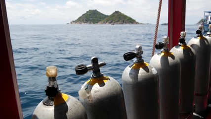 Row of oxygen tanks and diving equipment placed on modern boat in rippling ocean near Koh Tao...