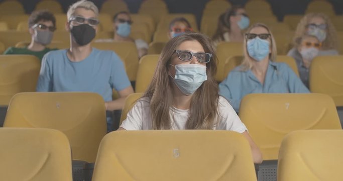 People in face masks watching 3d film in cinema on coronavirus quarantine. Film-lovers in 3d glasses sitting on yellow chairs and moving heads on Covid-19 pandemic. Cinema 4k ProRes HQ.