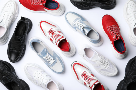 Many stylish sneakers on white background, top view