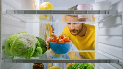 Inside Kitchen Fridge: Handsome Man Takes Cherry Tomatoes from Opened Fridge. Man Preparing Healthy...
