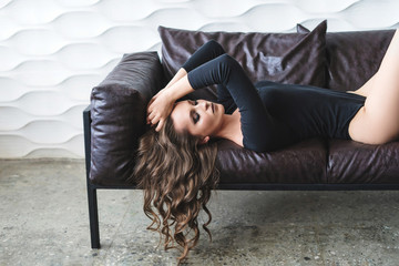 Sensual brunette woman with long curly hair posing on sofa. Women fashion.