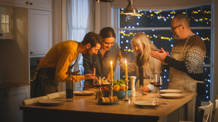 Happy Family of Celebrating together, Sitting at the Table with Delicious Dinner. Young Mother Takes Dish out of Oven Grandparents Admire How Delicious Casserole Looks